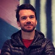 A portrait photograph of Head of Department Christopher Bennett. He wears a jacket and a red t-shirt.