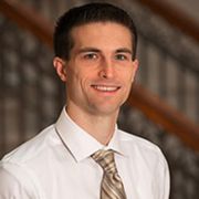 A portrait photo of philosopher T. Ryan Byerly. He is wearing a white shirt and patterned gold tie.