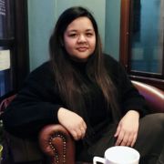 A photograph of Fasha Johanis sat on a leather armchair. On the table in front of her is a white mug.