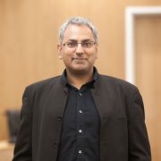 A head and shoulders photo of Kamal Birdi stood in the Middleton Lecture Theatre.