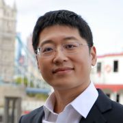 Image of a dark haired asian man wearing glasses, and a suit. He is outside and is smiling at the camera.