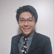 A man with dark hair and glasses is smiling at the camera, he is wearing a shirt and a tie with aeroplanes on.