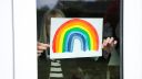 Senior woman holding rainbow drawing in window in support of national health service during Covid-19