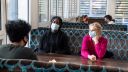 3 people sit at a table wearing face masks.