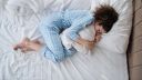 Top view of depressed woman in pyjamas lying in bed in bedroom. - stock photo