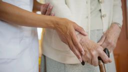 A carer with an elderly person holding a walking stick