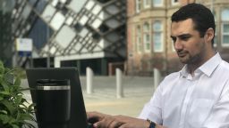 Photo of masters student Sammy Shaw working on a computer outside
