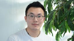 Guopeng Li sat in front of a plain white wall and a plant