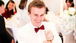Matthew Allcock in a shirt and bow tie sat at a table smiling