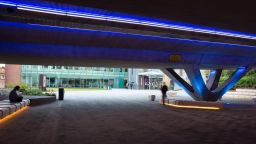 The refurbished concourse on campus. Taken from underneath the concourse, the photo shows the blue neon lights on the ceiling and yellow neon lights around the bottoms of seating areas.