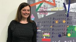 A member of staff stood alongside a multilingual poster