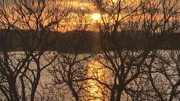 A scene of the sun and trees and water
