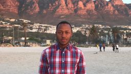A profile photo of alumni, Saleh. He is wearing a plaid shirt and standing in front of some red rocks. 