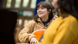 student smiling and playing cello with pianist 