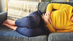 A picture of a woman laid on a sofa clutching her stomach in pain.