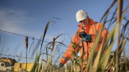 Man in a high visibility coat and hat in a field using a smartphone to get data from the soil