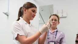 A nurse apprentice preparing to administer an injection under supervision from their tutor