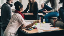 A group of people sat round a table working together. On the table is stationery and papers.