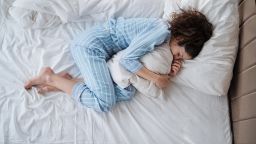 Top view of depressed woman in pyjamas lying in bed in bedroom. - stock photo