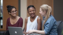 A group of students talking in the Library around a laptop.