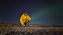 Image of IR & Politics student crouched in front of the Northern Lights in Sweden