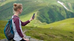 Photograph of a young woman sitting on a rock looking into her phone