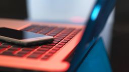 A close up of a mobile phone placed on the keyboard of a laptop