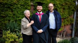 Aidan, a graduating clinical neurology student, with his parents outside a Sheffield building.