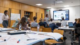 Students sit in a seminar room, facing an interactive whiteboard