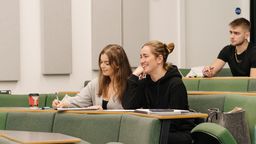 two Caucasian women sit next to each other in a lecture hall