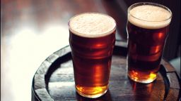 Two pints of beer on a wooden barrel inside a pub