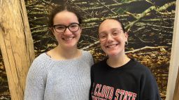 Two young women smiling at the camera standing in front of a nature poster