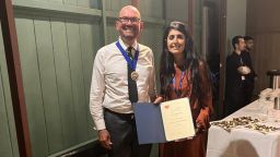 Hanya Mahmood holds up an award. A man stands next to her in a white shirt and black trousers.