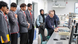A group of five male students wearing school uniforms watch Professor Chris Stokes show them something on a computer screen.
