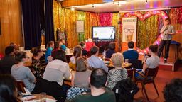 People sat around tables watching a scientist give a talk on stage