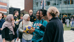 Group of people chatting, one holding a netball.