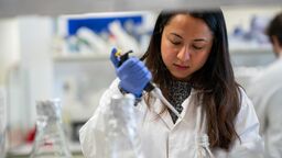 A person in a lab, wearing a lab coat, carrying out scientific tests.